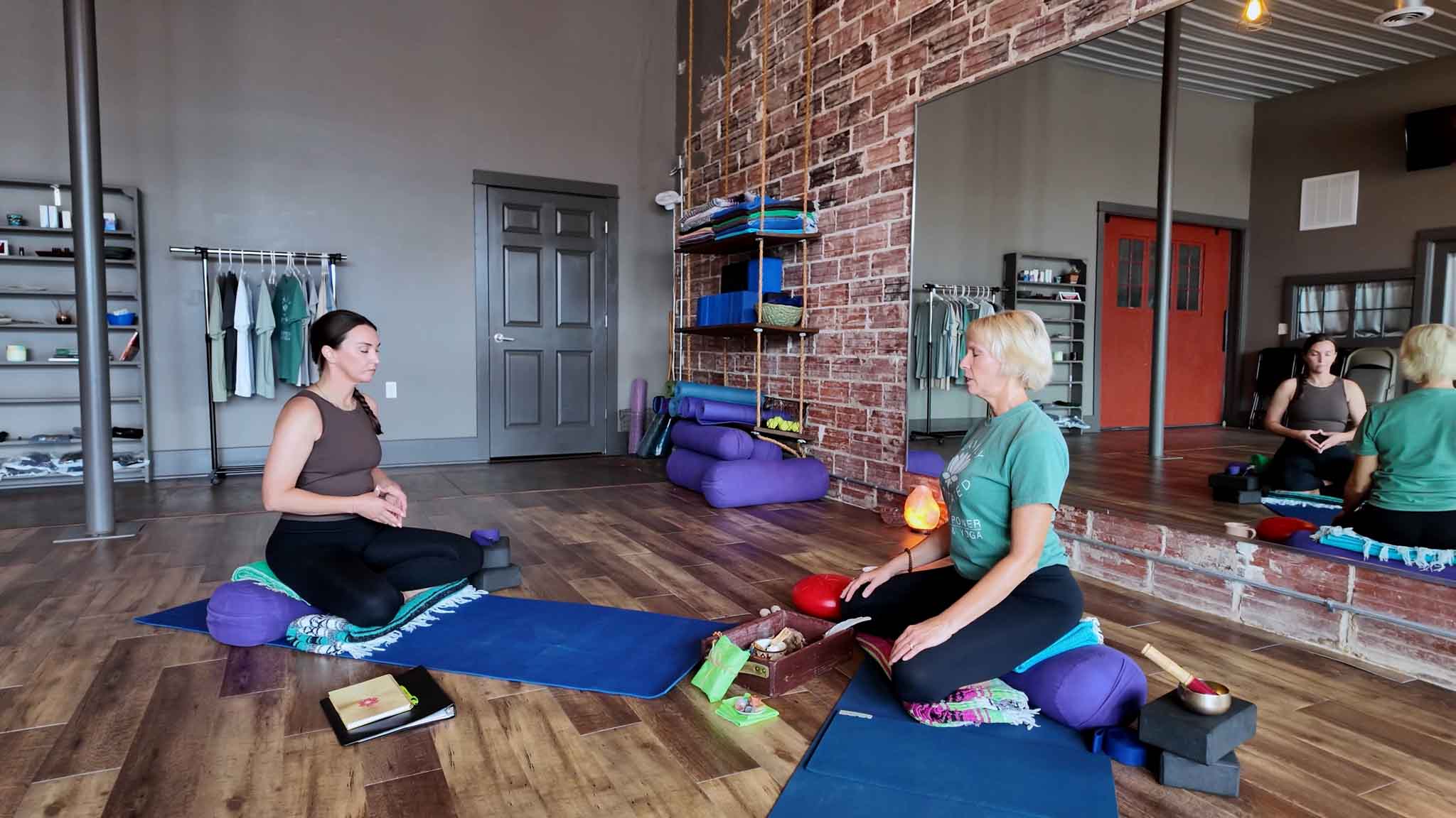 Michelle Robert sitting cross-legged with a student in the Higher Power Health studio, both settling into a meditation.